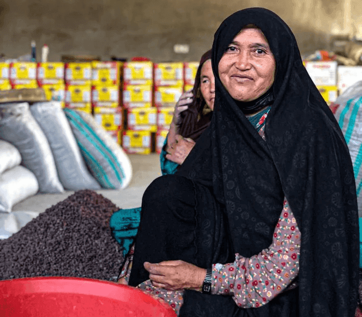 Picture of a smiley afghan woman working with dried fruits.